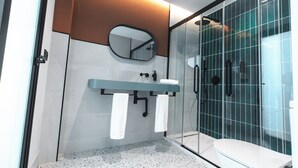 Un baño moderno con cabina de ducha de vidrio, un lavamanos blanco con un espejo encima y un perchero con toallas blancas.