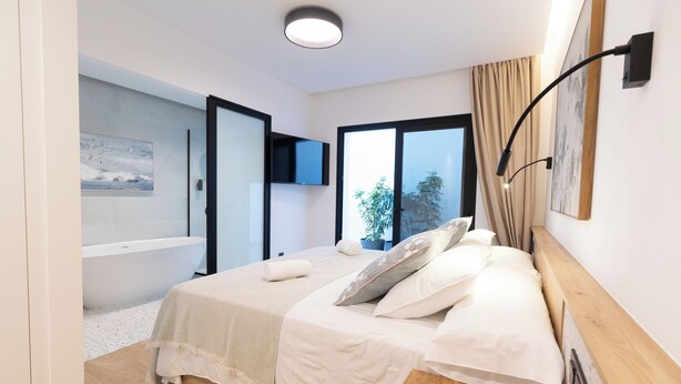 Un dormitorio moderno con una cama grande, un televisor de pantalla plana montado en la pared y vistas al exterior a través de un amplio ventanal.