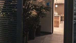 Un pasillo moderno con una planta en maceta, un banco de madera y un acceso a una habitación con zona de comedor.