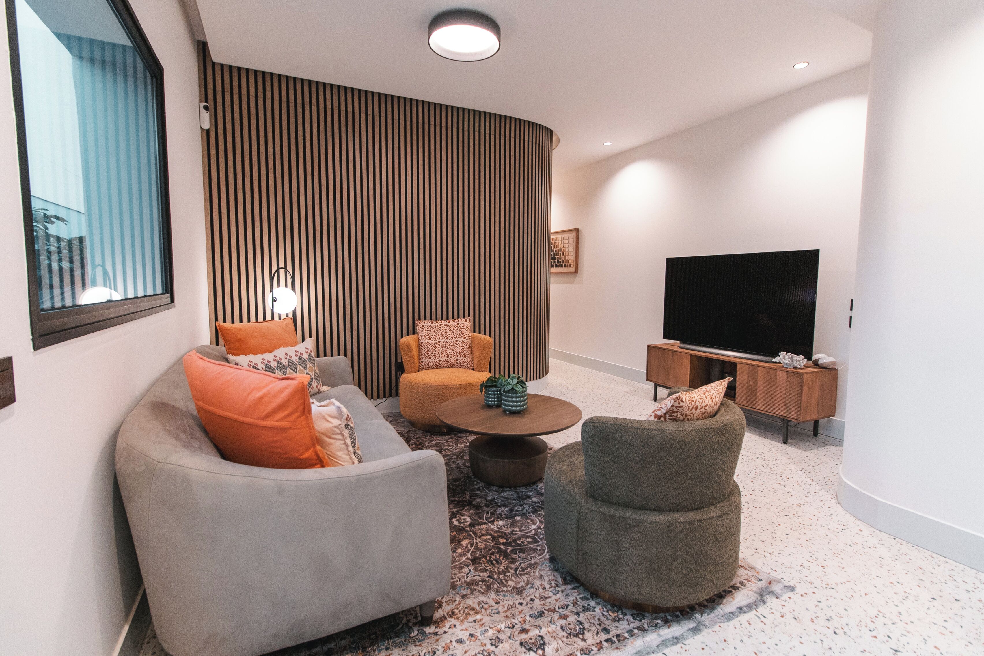 A modern living room with a sofa, armchair, and ottoman, a coffee table, a TV, and a wooden accent wall.