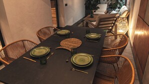 Un espacio exterior para comer con una larga mesa preparada para seis personas, rodeado de sillas de mimbre.