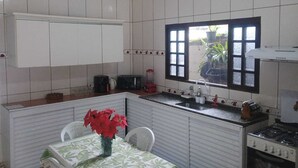 Eine Küche mit weißen Schränken, einem Fenster mit schwarzen Rahmen, einem Gasherd und einem Esstisch mit Stühlen.
