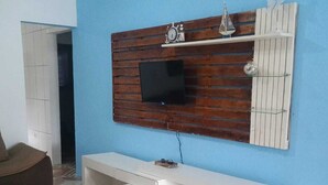 Ein Wohnzimmer mit an einer Holzpaneelwand montiertem Fernseher, einer weißen Unterhaltungseinheit darunter und gemusterten Bodenfliesen.