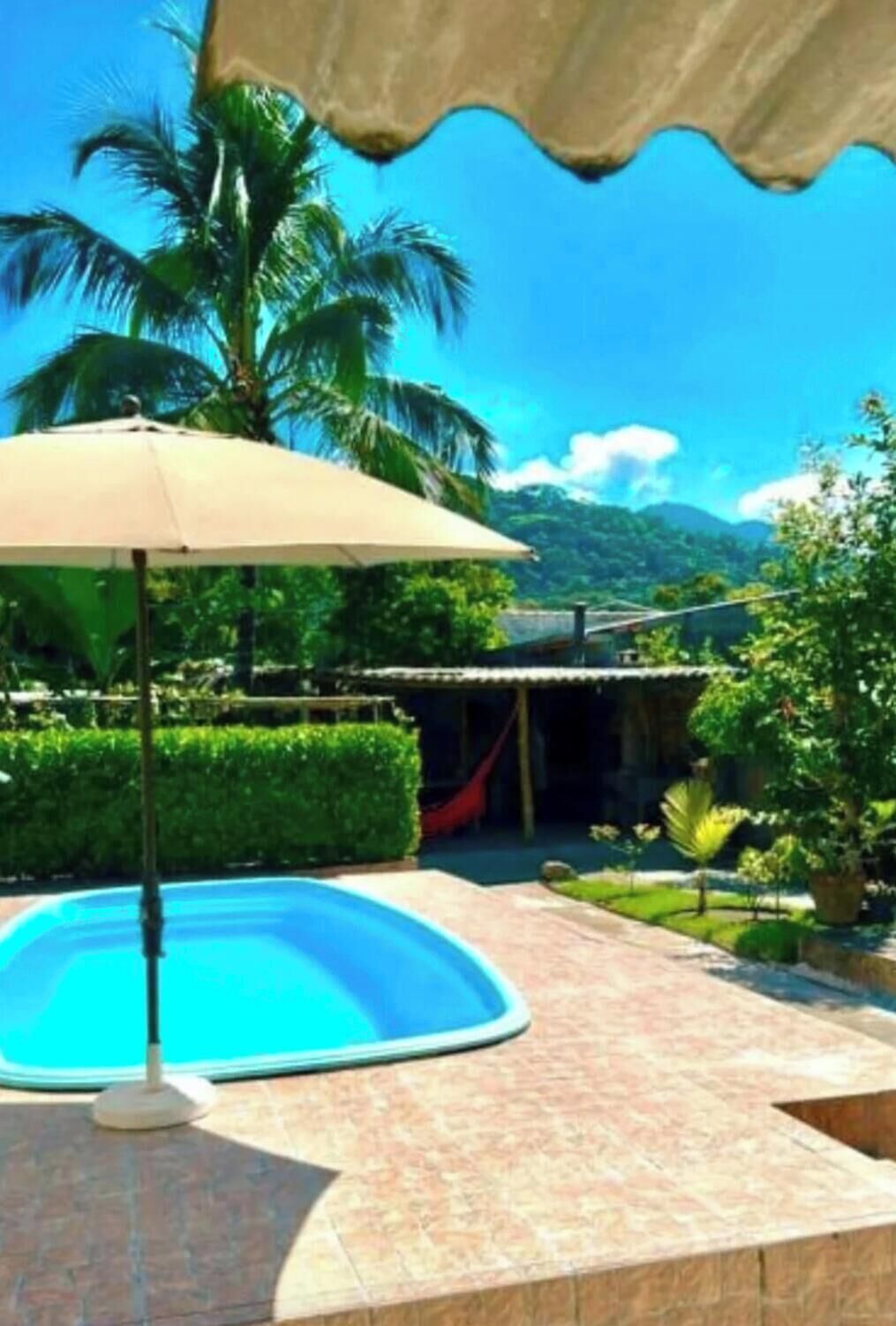 A swimming pool with a beige umbrella, surrounded by greenery and a view of mountains.