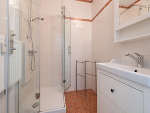Ein modernes Badezimmer mit Duschkabine aus Glas, einem weißen Waschbecken und Fliesenboden.