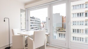 A modern apartment with a dining area, large windows, and a view of city buildings. - Apartment With Side sea View (Ostend)