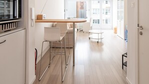 A modern kitchen with a microwave, a wooden table, and a bar stool. There is a white chair and a small round table in the dining area. - Apartment With Side sea View (Ostend)