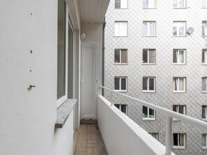 Ein schmaler Balkon mit weißer Geländer, einer Tür und einem Fliesenboden.