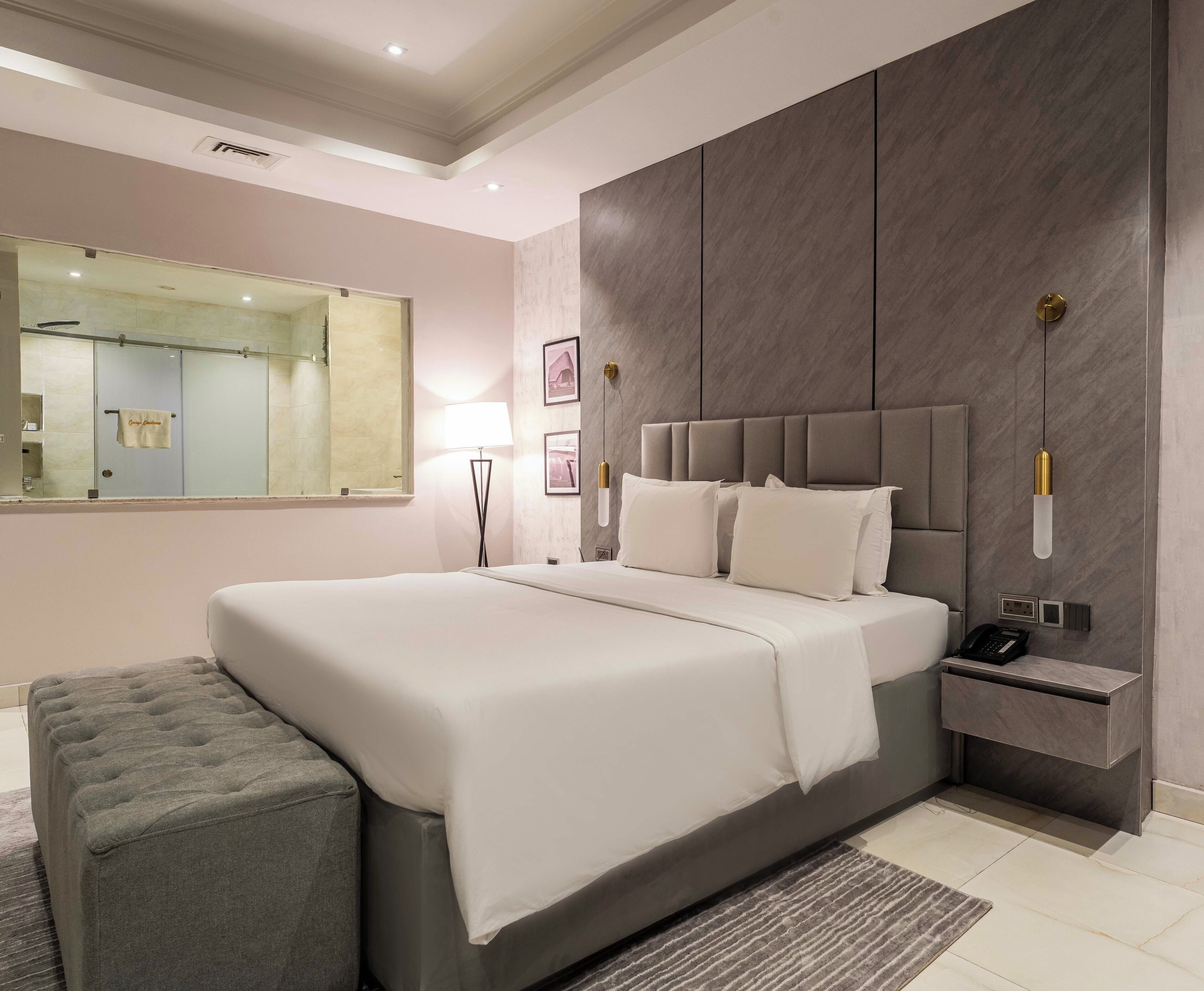 A modern bedroom with a large bed, a bedside table, a nightstand, a lamp, and a mirror.