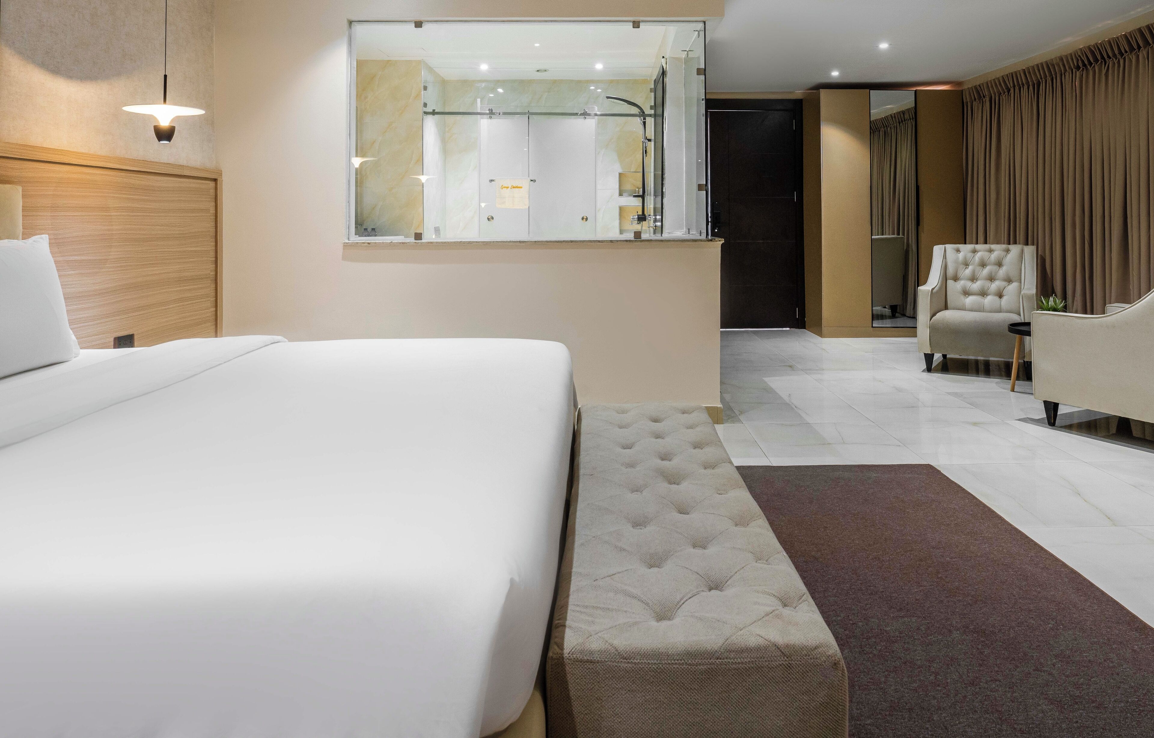 A modern hotel room with a large bed, a seating area with a chair, a small table, and a mirror.