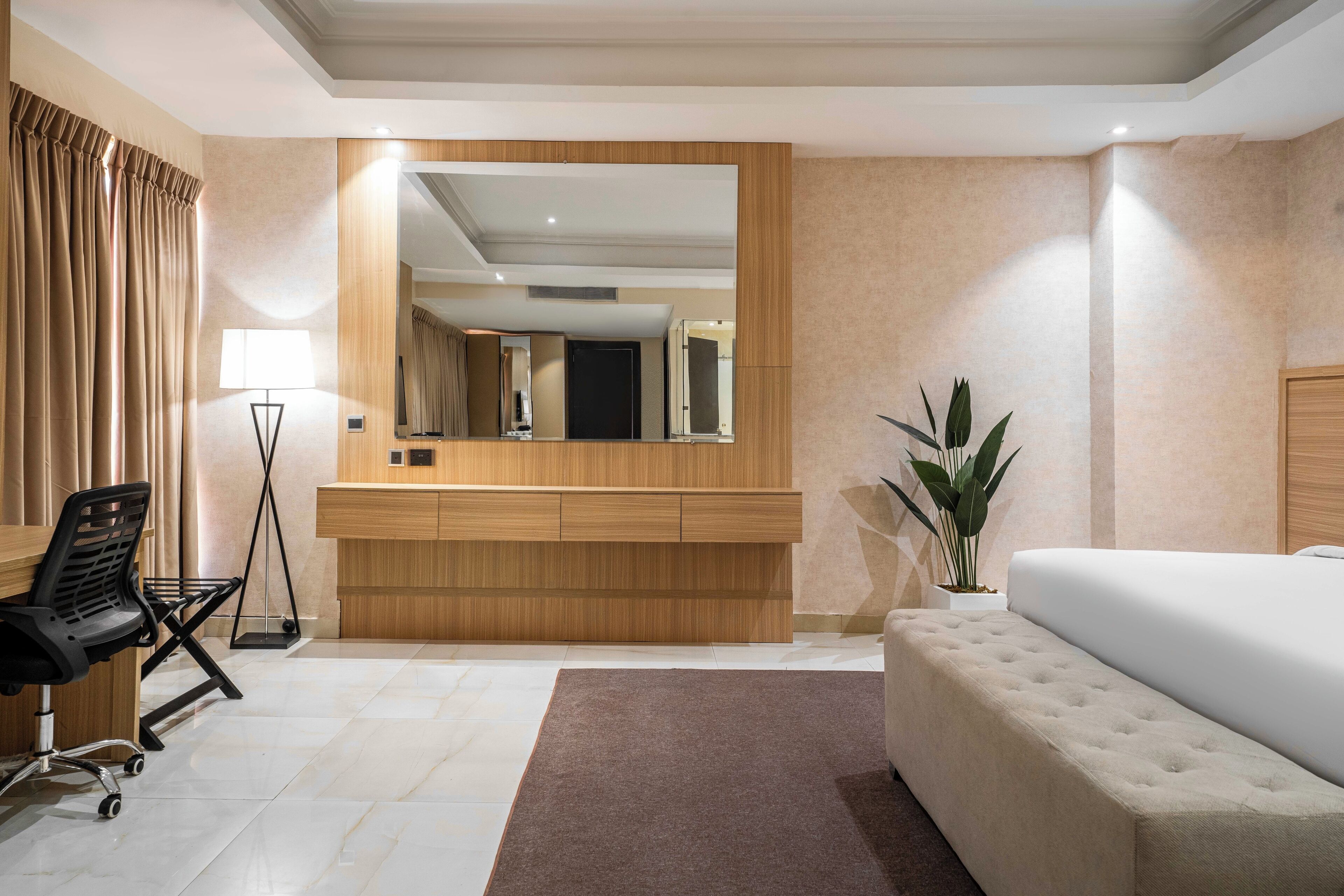 Une chambre d’hôtel moderne avec un grand lit, un bureau avec une chaise, un miroir et une plante en pot.