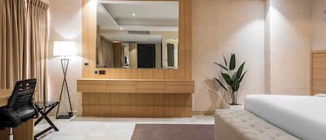 A modern hotel room with a large bed, a desk with a chair, a mirror, and a potted plant.