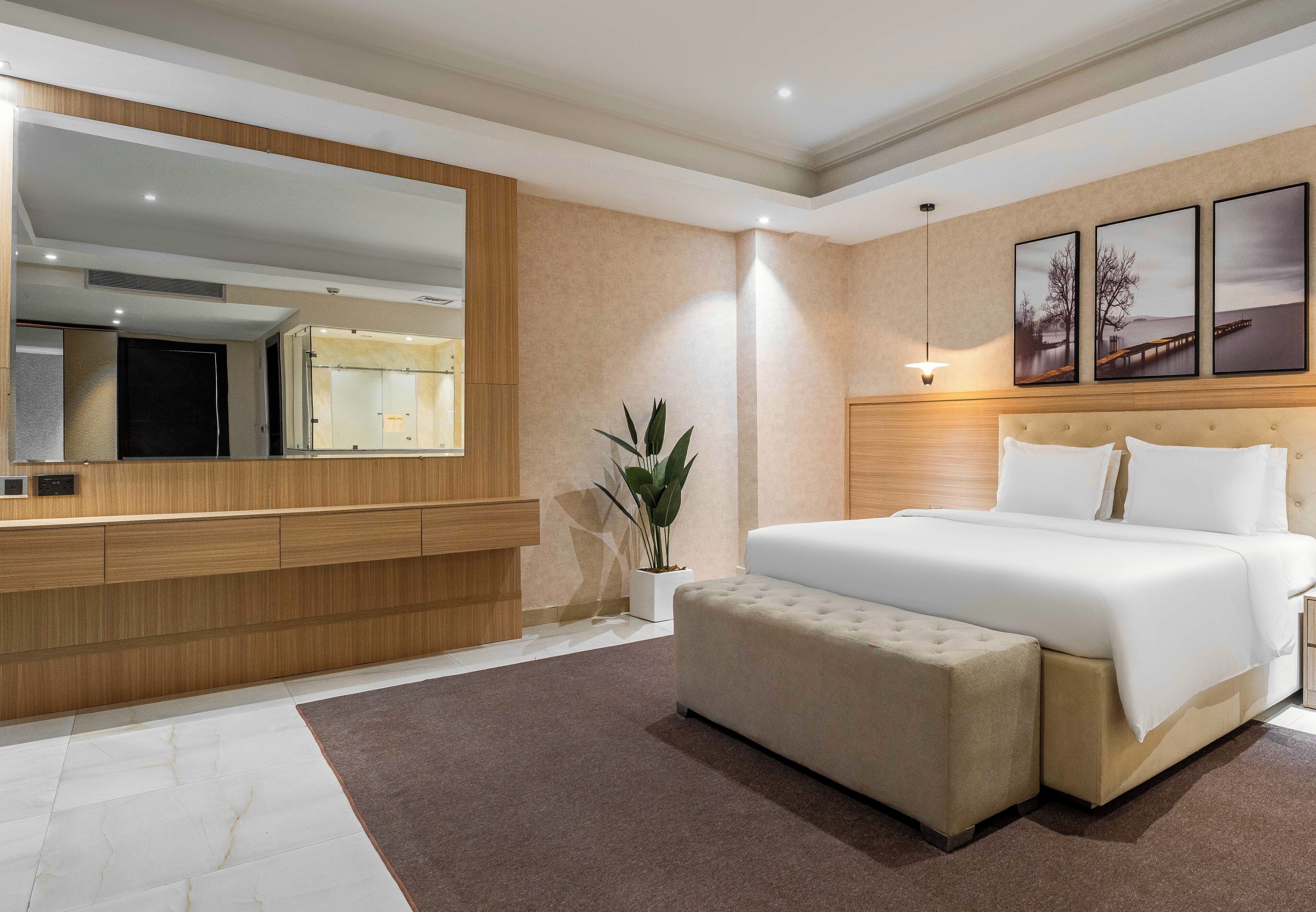 Una habitación de hotel moderna con una cama grande, una mesita de noche, un espejo y una obra de arte colgada en la pared.