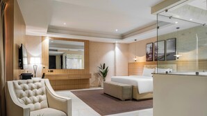 Een moderne hotelkamer met een groot bed, een zithoek met een stoel en een klein tafeltje, een grote spiegel en een badkamer zichtbaar door een geopende deur.