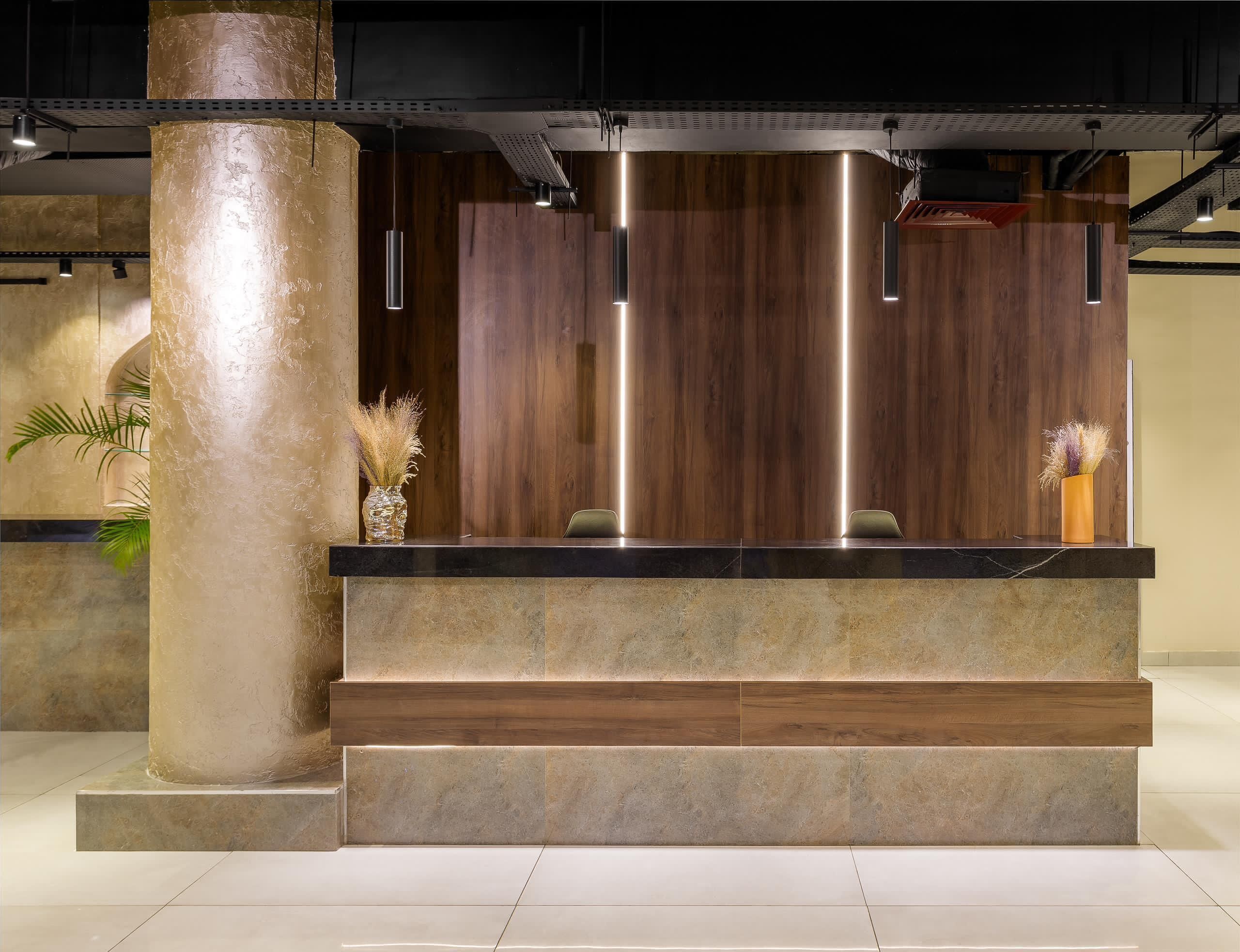 A reception desk with a wooden backdrop, a large pillar, and a vase with dried plants.
