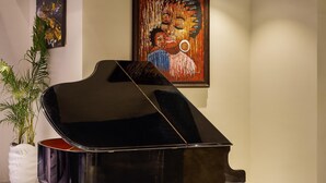 Een vleugelpiano in een goed verlichte kamer met een schilderij aan de muur en een kamerplant.
