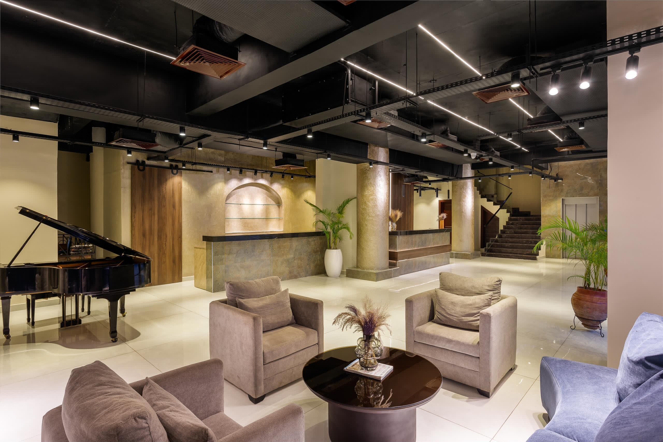 A spacious lobby with a grand piano, comfortable seating, a staircase, and a reception desk.
