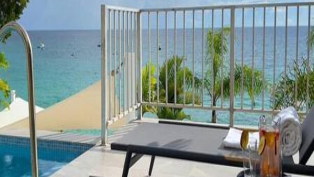A poolside area with a view of the ocean, a lounge chair, and a glass of drink.