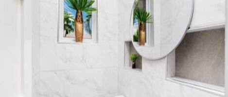 Une salle de bain équipée de toilettes, d’un lavabo et d’une fenêtre donnant sur des palmiers.
