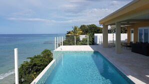 A swimming pool with a view of the ocean, a covered patio area, and a white fence. - Je Suis Jamaica - 4 B R Beachfront Villa w Staff (Duncans)