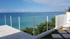 A coastal view with a white fence, a paved walkway, and a clear blue sky. - Je Suis Jamaica - 4 B R Beachfront Villa w Staff (Duncans)