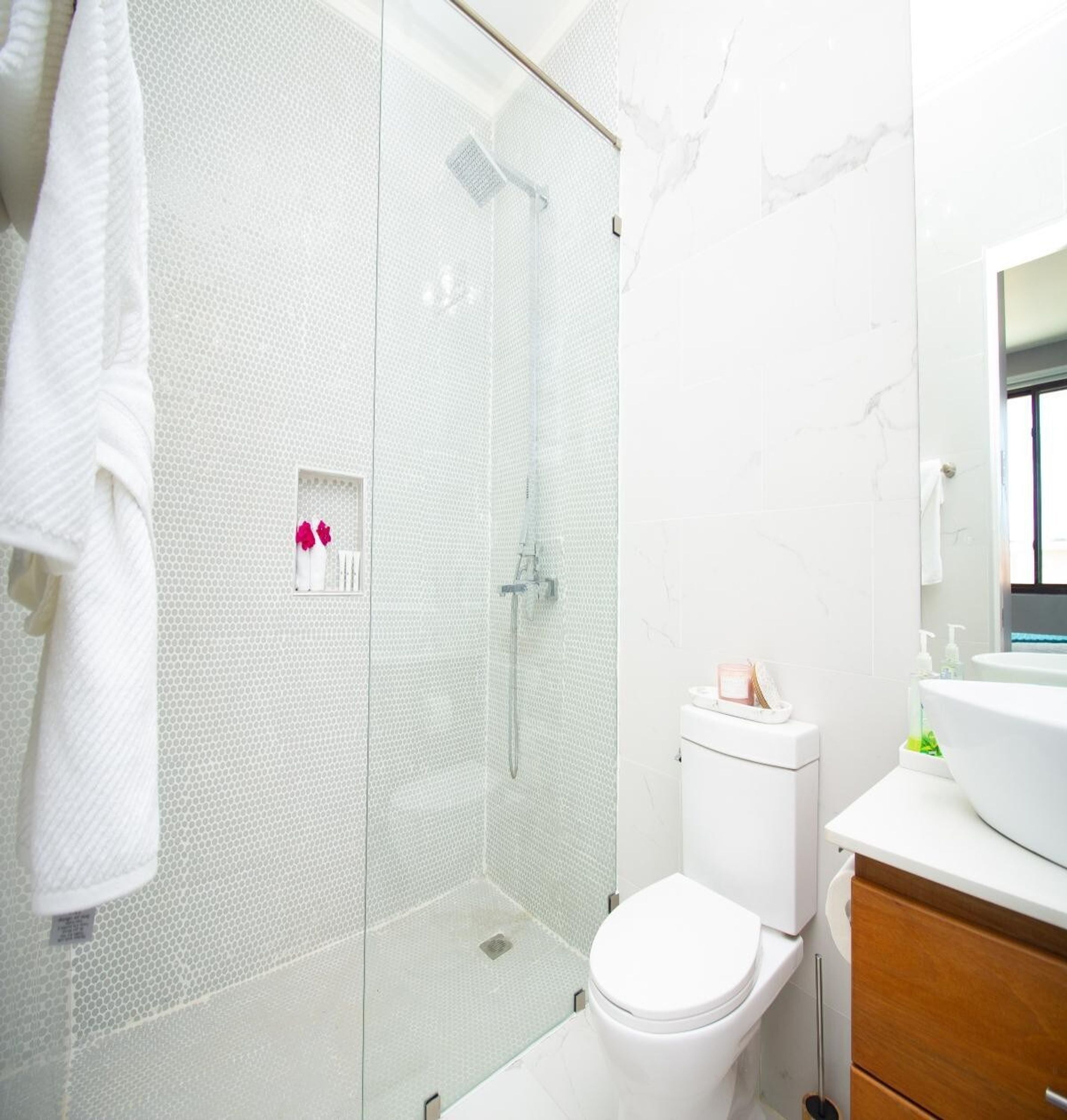Une salle de bain moderne avec une douche à parois de verre, des toilettes blanches et un meuble-lavabo avec un miroir.