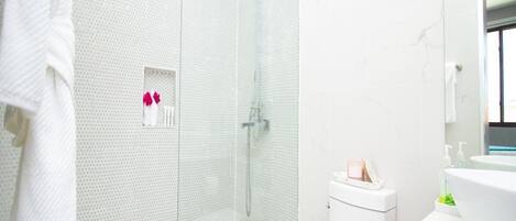 Une salle de bain moderne avec une douche à parois de verre, des toilettes blanches et un meuble-lavabo avec un miroir.