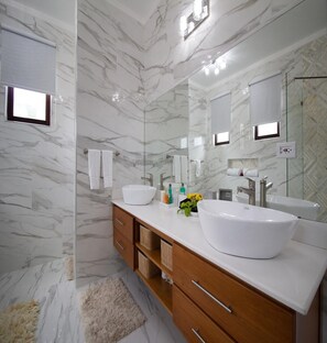 A modern bathroom with marble walls, two sinks, a large mirror, and a fluffy rug.