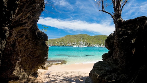 A beach with clear turquoise water, a sandy shore, and a view of a distant town. - Turtle Point Bequia - 4 B R Villa w Staff (Bequia Island)
