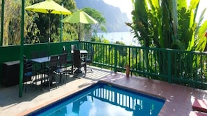 A pool area with a view of mountains, green umbrellas, and outdoor seating. - Turtle Point Bequia - 4 B R Villa w Staff (Bequia Island)