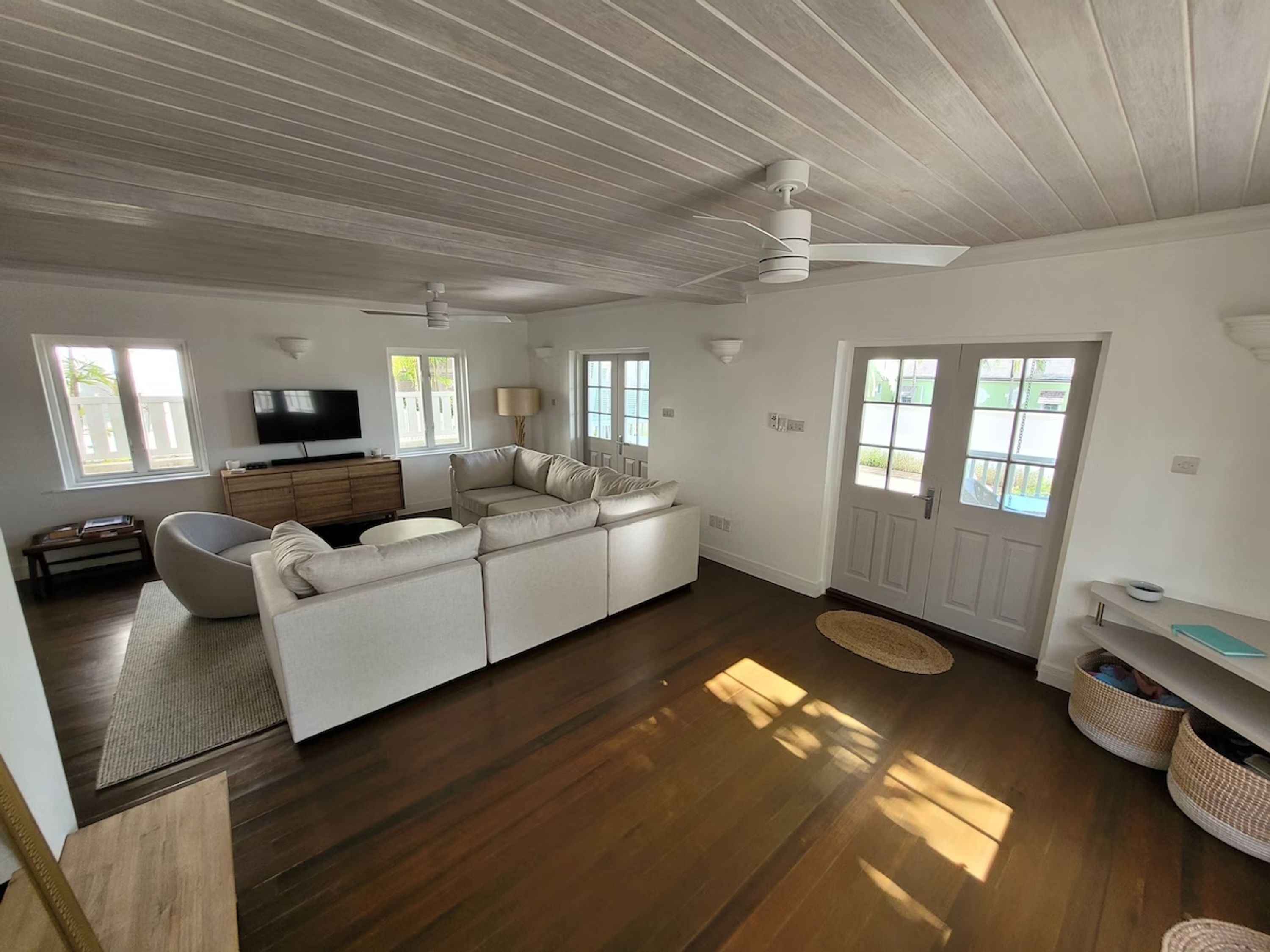 A modern living room with a large white sofa, a flat-screen TV, and a ceiling fan.