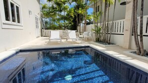 Una piscina con bordeado de baldosas, rodeada de palmeras y sillas blancas.