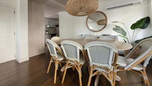Un comedor con una mesa redonda, seis sillas de mimbre, una lámpara colgante tejida y un espejo grande en la pared.