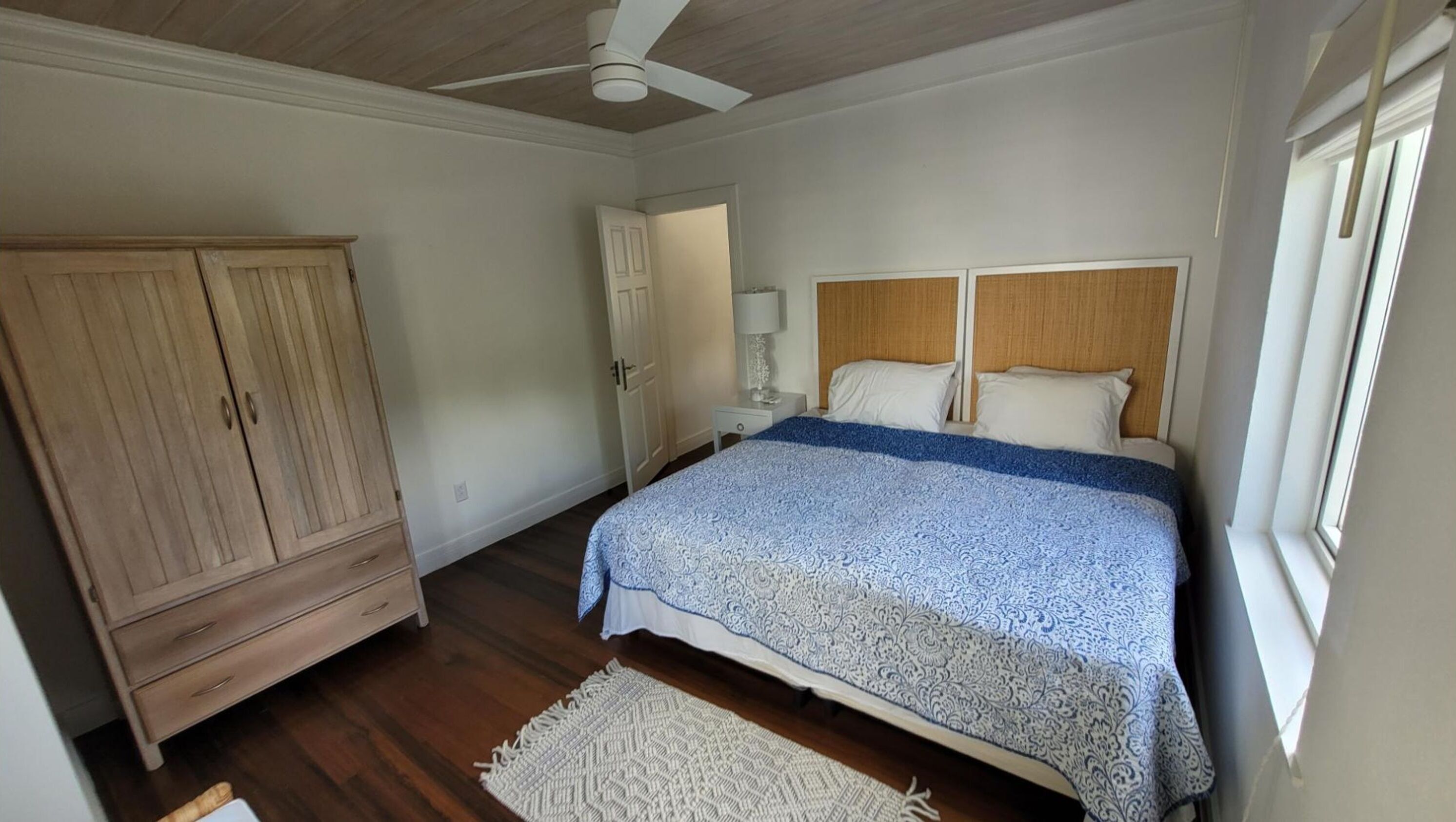 Ein Schlafzimmer mit einem Bett, einem Holzschrank, einem Nachttisch, einer Lampe und einem Fenster.