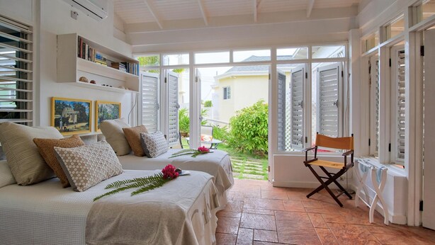 Ein Schlafzimmer mit zwei Betten, einem Sessel und Blick auf den Garten durch geöffnete Fensterläden.