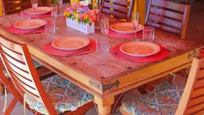 A dining table set with red plates and glasses, surrounded by wooden chairs with patterned cushions. - Flamingo Bequia - 4 B R Villa Including Cottage (Bequia Island)