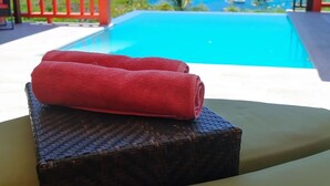 A poolside area with a table and a rolled-up towel, overlooking a clear blue ocean with boats. - Flamingo Bequia - 4 B R Villa Including Cottage (Bequia Island)