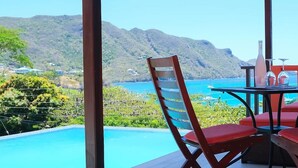 A poolside area with a table and chairs, overlooking a mountainous landscape and a body of water. - Flamingo Bequia - 4 B R Villa Including Cottage (Bequia Island)