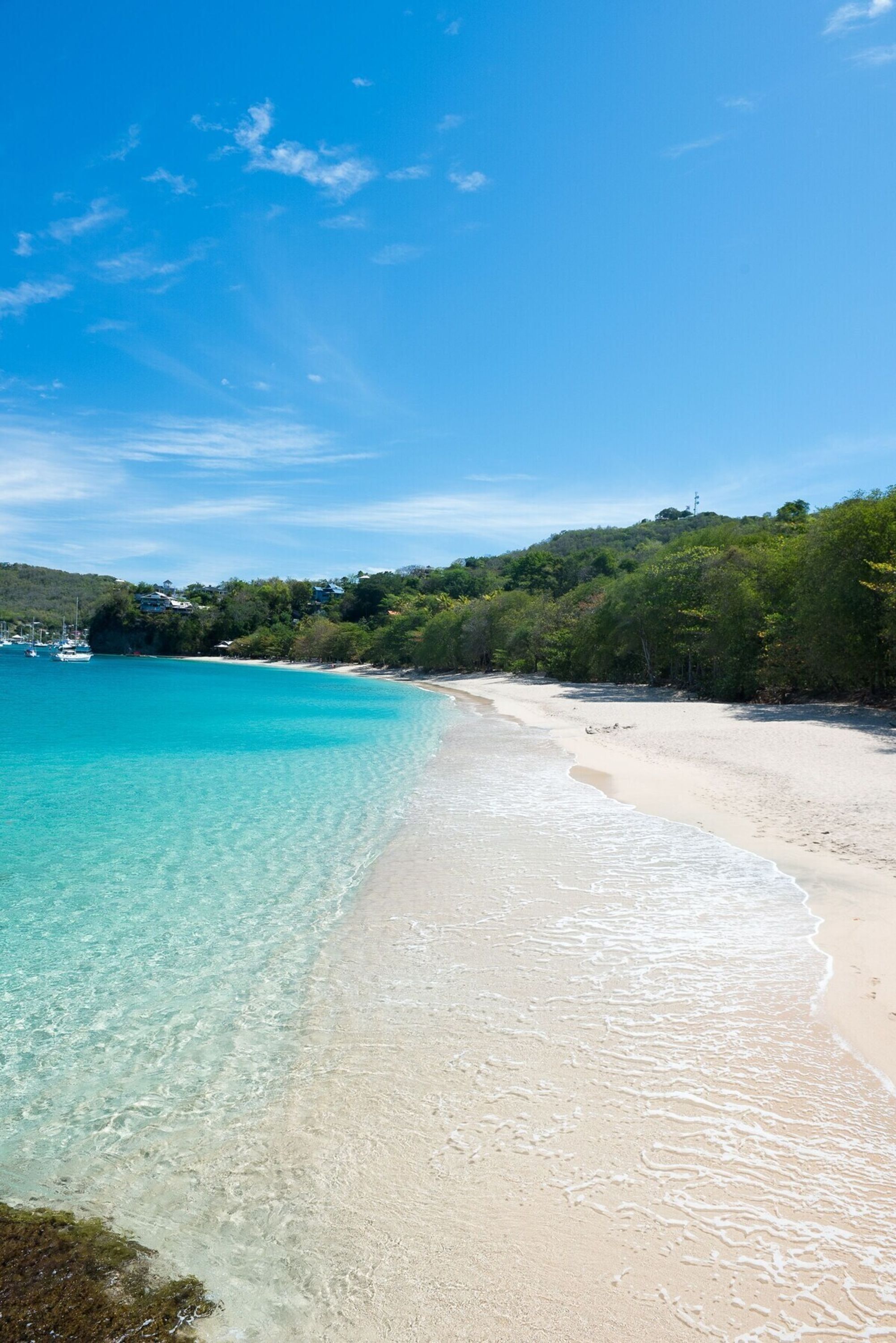 Una playa con agua turquesa cristalina, orilla de arena y vegetación al fondo.