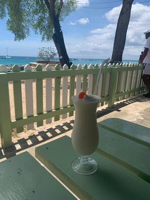 Une boisson sur une table verte, avec une clôture blanche en bois et une plage en arrière-plan.