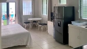 A hotel room with a bed, a small dining table with chairs, a refrigerator, and a kitchenette area. - The Art Studio 12 Beachfront Apartment Barbados (Holetown)
