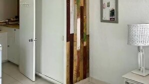 A room with a white refrigerator, a wooden wall panel, a framed picture, and a lamp on a table. - The Art Studio 12 Beachfront Apartment Barbados (Holetown)