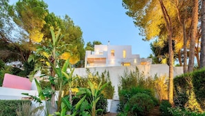 A modern house with a white exterior, surrounded by lush greenery and trees.