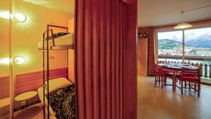 Ein Zimmer mit einem Etagenbett, einem kleinen runden Tisch mit Stuhl, einem Esstisch mit vier Stühlen und Blick auf einen Berg durch große Fenster.