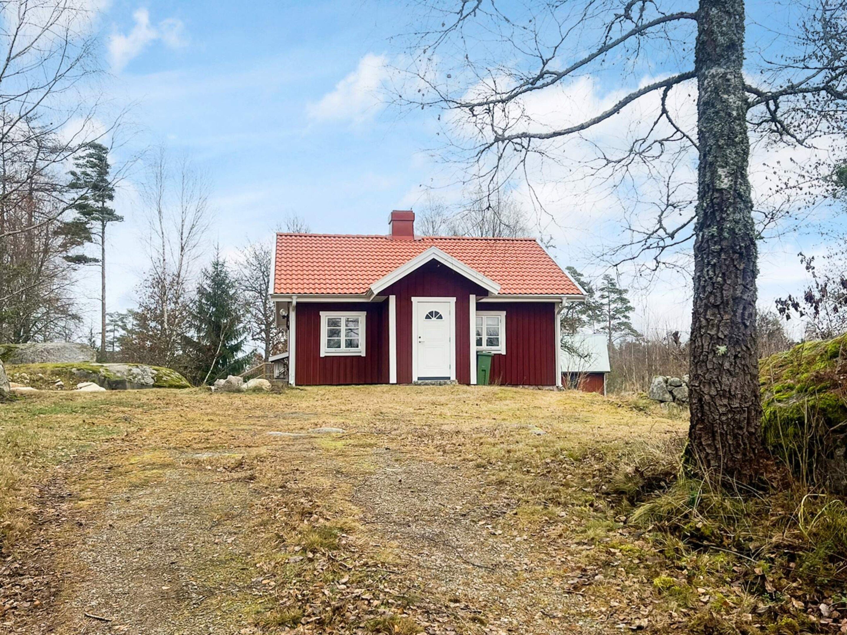 Una casa de madera roja con puerta y ventanas blancas, rodeada de árboles y un camino de grava.