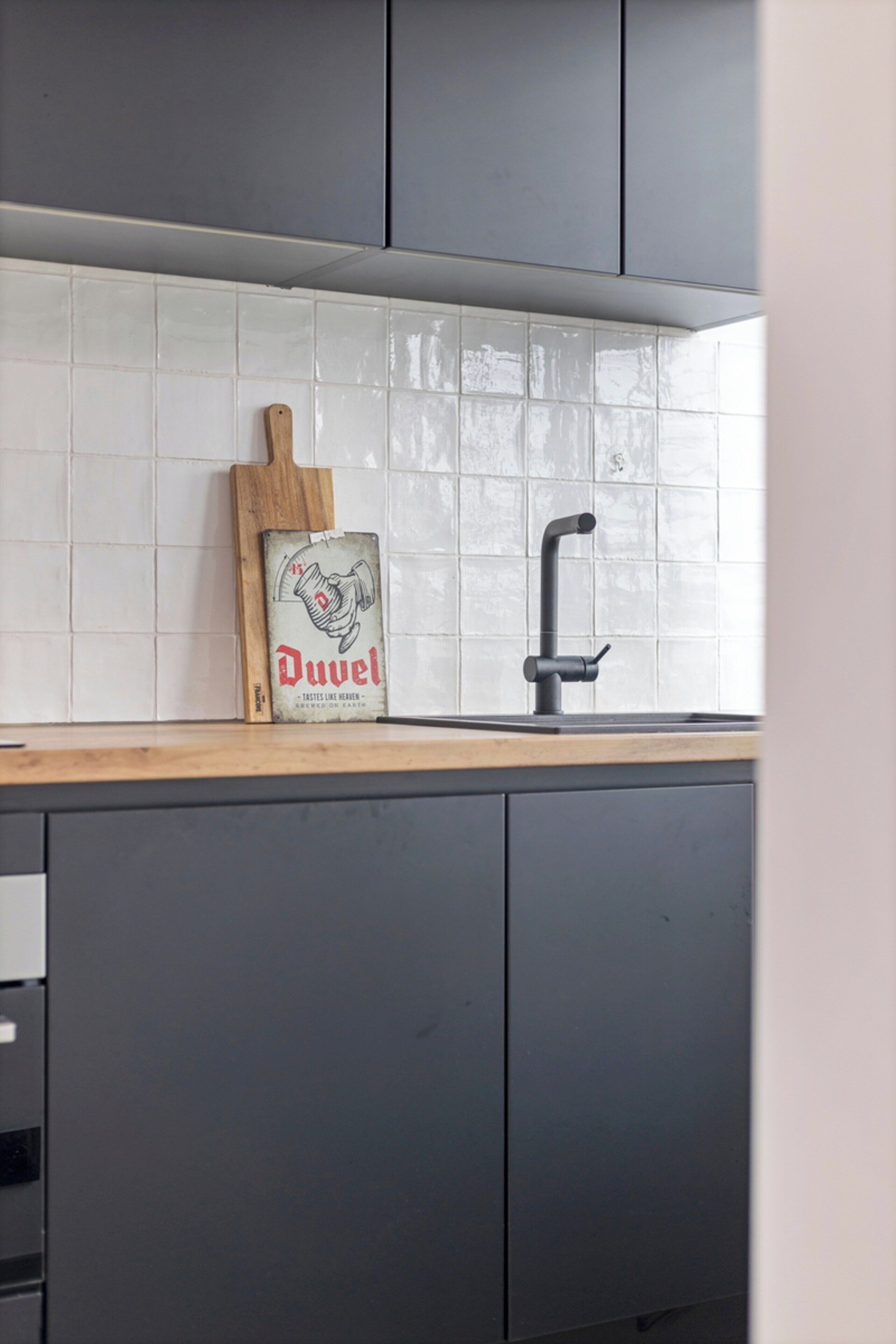 A kitchen with a tiled backsplash, a wooden cutting board, and a black faucet.