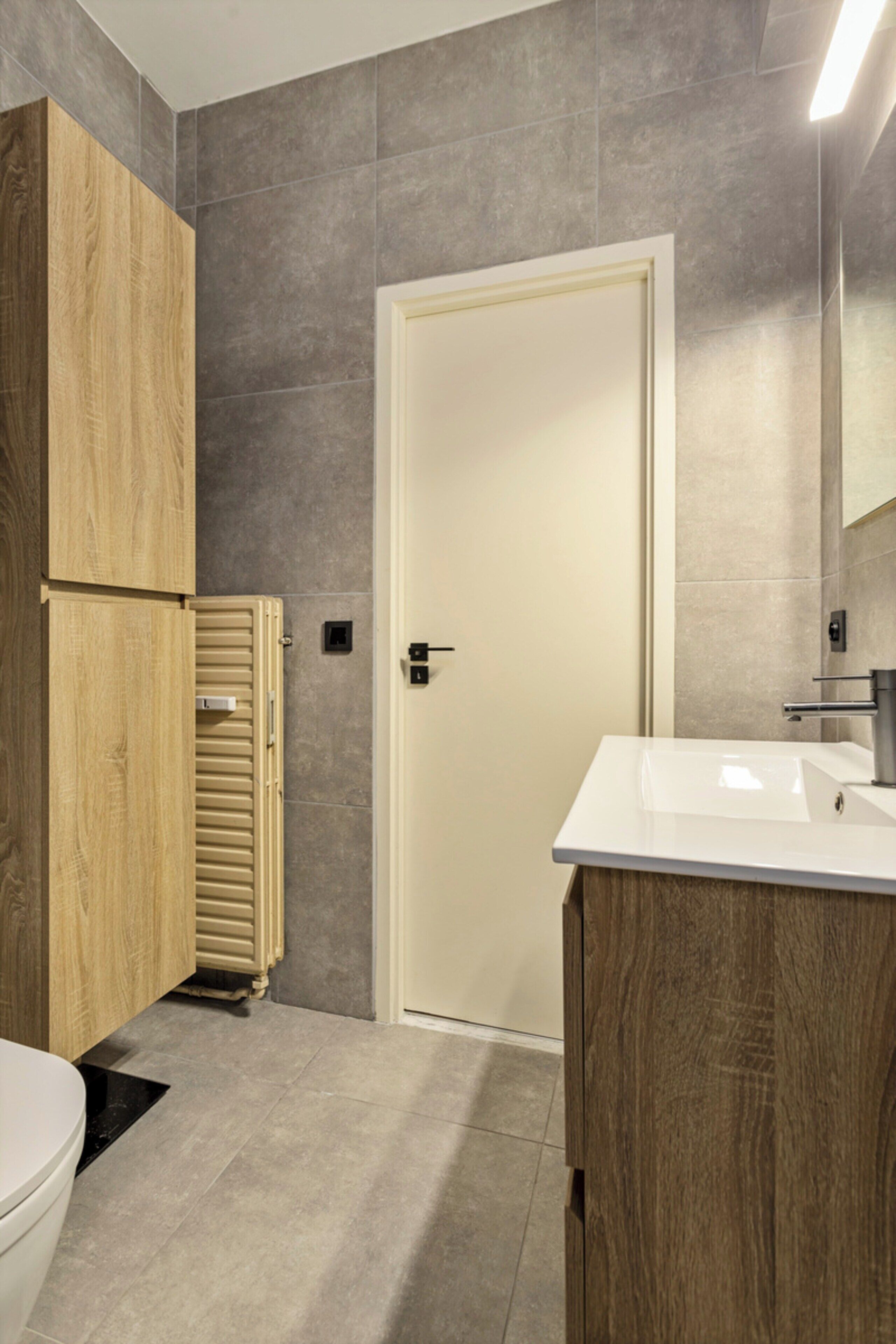 A modern bathroom with a wooden cabinet, a white sink, and a door.