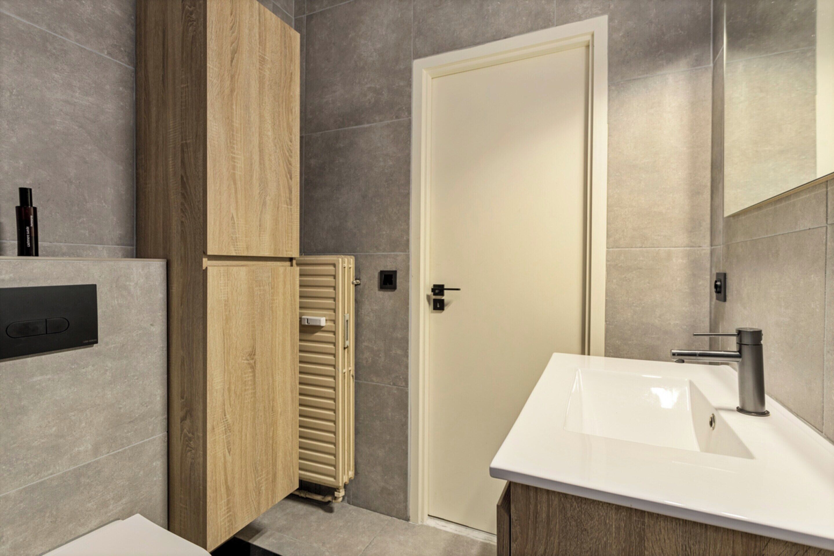 A modern bathroom with a wooden cabinet, a white sink, and a door.