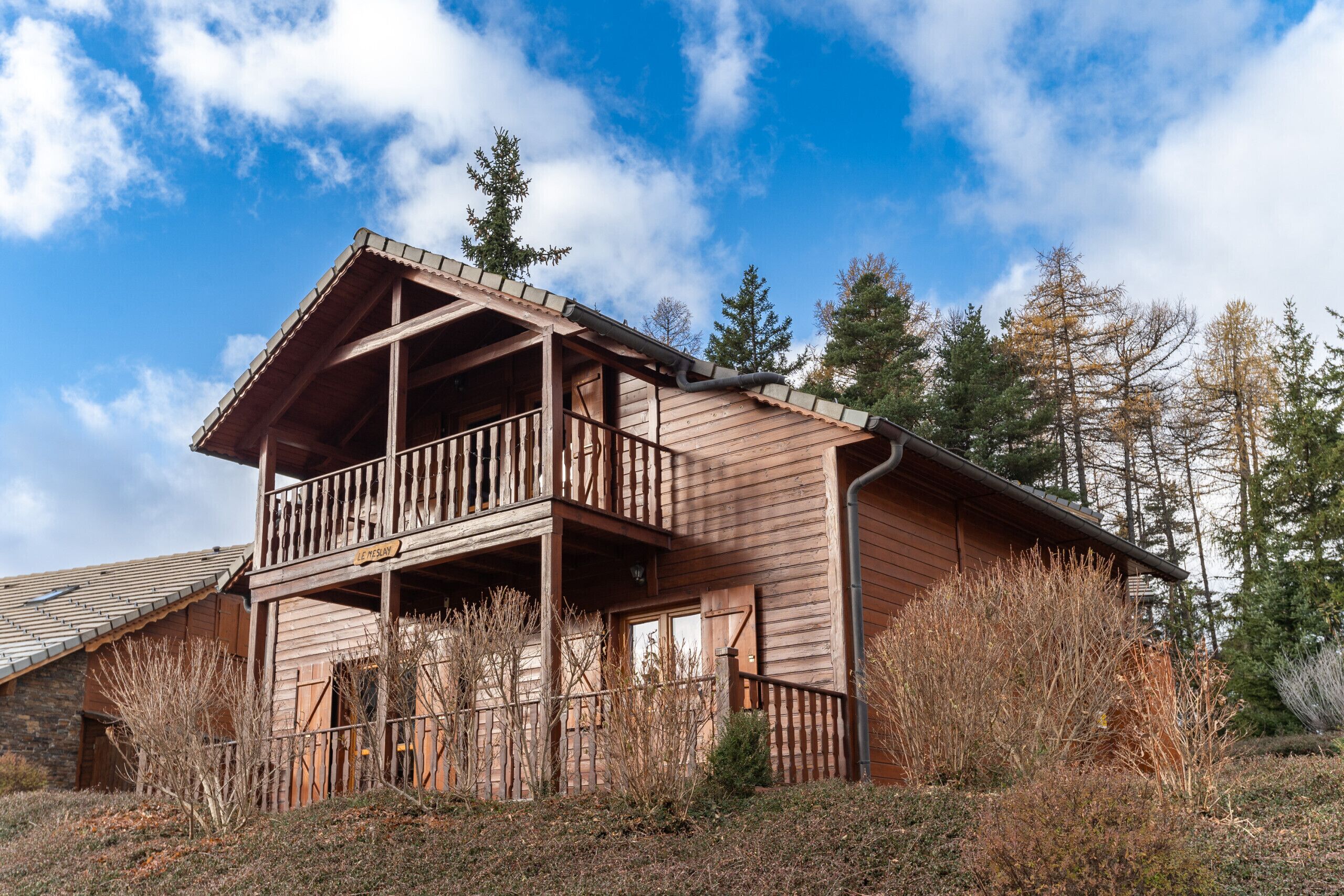 A wooden cabin with a balcony, surrounded by trees and a clear sky.