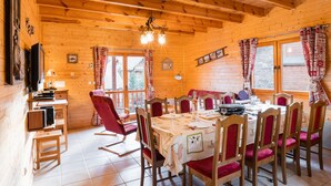 Una baita in legno con zona pranzo che include un tavolo rotondo, sedie imbottite rosse e un lampadario.